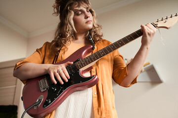 Obraz premium Female musician feeling involved while playing guitar at home at her room