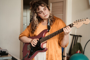 Female musician feeling involved while playing guitar at home at her room
