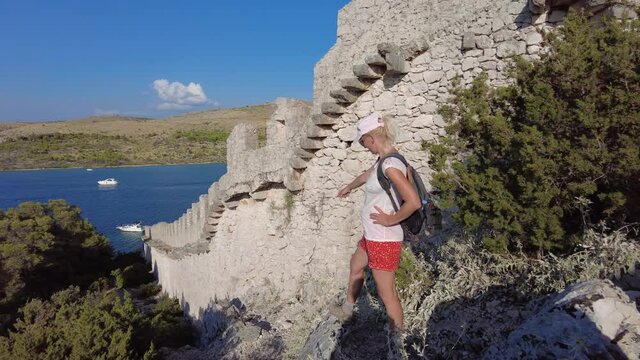 Woman on the Wall of Ostrica, over Grebastica town with boats on the sea. Bedem Grebastica historic defensive wall of Croatia in Croatian-Ottoman wars. Grebastica village in Sibenik-Knin County.