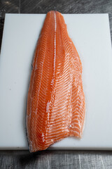Thick and juicy raw salmon fillet on a white plastic board