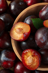 Wooden bowl with plums on plums background