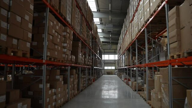 Modern logistics facility from inside, one of aisles between racks with shelves full of goods in cardboard boxes. Indoors warehouse filled with products ready for delivery to customers