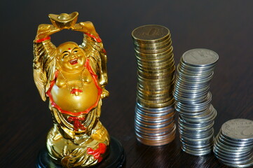 Figure of the Golden Buddha on the table. Next to it is a stack of coins. Symbol of wealth and prosperity.