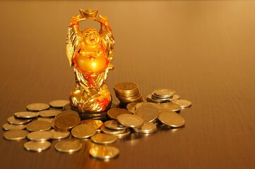 Figure of the Golden Buddha on the table. Next to it is a stack of coins. Symbol of wealth and prosperity.