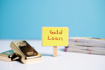 Concept of gold loan showing wiyh Gold loan sign board with Gold bars and currency notes on table.