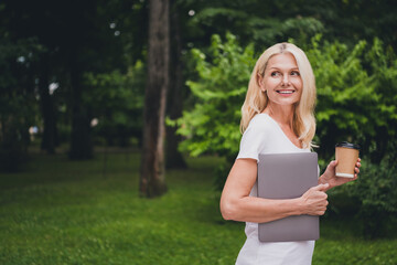 Profile photo of aged business blond lady hold laptop coffee wear white t-shirt in park alone