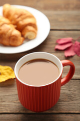 Hot coffee with croissant and autumn leaves on grey - seasonal relax concept. Vertical photo
