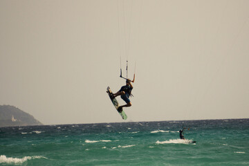 Young male grabbing his board during a jump in kitesurfing - obrazy, fototapety, plakaty
