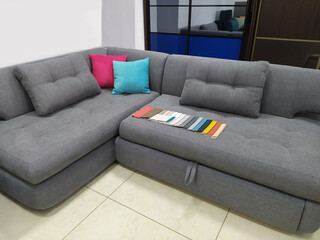 Beautiful modern gray sofa with pink and yellow cushions and with сolorful and bright curtains fabric pattern palette texture samples . Sofas in the furniture showroom. Sale of sofas