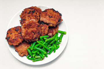 on a white background in a plate next to the cutlets lies green string beans; the choice between carcinogens in fried meat and the beneficial properties of legumes; the photo contains a copy space