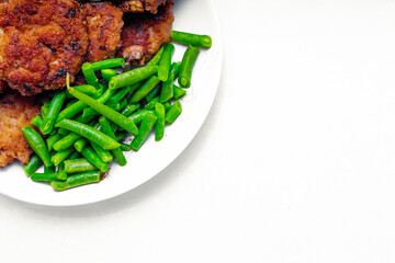 on a white background in a plate next to the cutlets lies green string beans; the choice between...