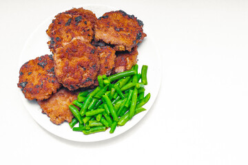 on a white background in a plate next to the cutlets lies green string beans; the choice between...