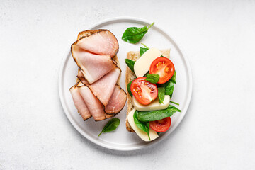 Baguette sandwich with ham, spinach, tomatoes and mozzarella cheese. Snack healthy fast food, top view, light background