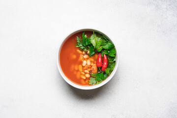 Vegetarian bean soup with tomato, hot peppers and green parsley. Vegan stew with legumes and vegetables. White background, top view
