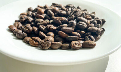 Black arabica fragrant coffee beans on the white plate.	