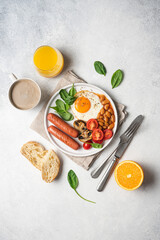 Traditional English breakfast with fried egg, beans in tomato sauce, grilled sausages, mushrooms and fresh tomatoes, served on plate. White background^ flat lay