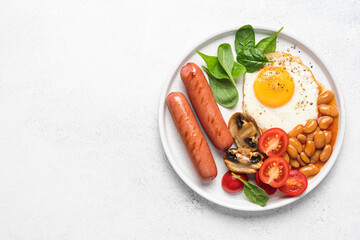 Traditional English breakfast with fried egg, beans in tomato sauce, grilled sausages, mushrooms and fresh tomatoes, served on plate. White background^ flat lay
