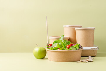 Healthy vegetable salad in recyclable cardboard container. Food delivery, healthy food menu for home or office concept. Green background, side view
