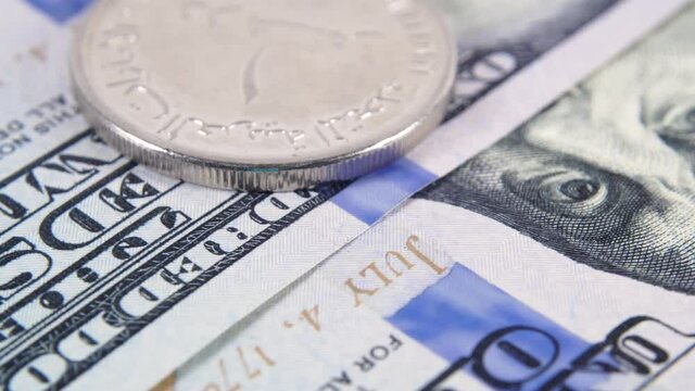 Stack of United Arab Emirates coins against the background of US hundred dollar bills. Pegged exchange rate concept. Macro view. Rotating money background. UAE money on american dollars. UAE exchange.