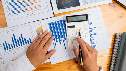 top view businessman holding pen to analyze and discuss and brainstorm data chart financial report concept work consulting office An accountant working on a desk using a calculator to calculate financ