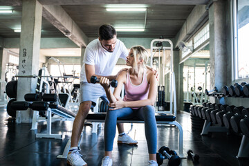 Sport women lifting dumbbell with trainer men in gym