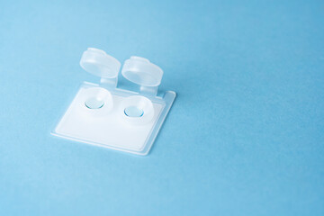 Hard contact lenses in plastic transparent container on a blue background. Myopia astigmatism correction. Ophthalmologist accessories.