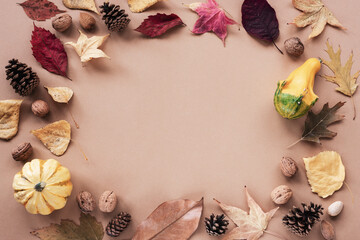 Frame of autumn leaves, walnuts, cones and pumpkins on brown background with copy space. Top view, flat lay