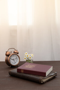 Bible and notebook on the table with an alarm clock by the window. Vertical format