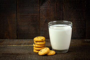 Closeup glass of milk with chocolate chip cookie on rustic wooden background.