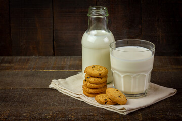 Closeup glass of milk with chocolate chip cookie on rustic wooden background.