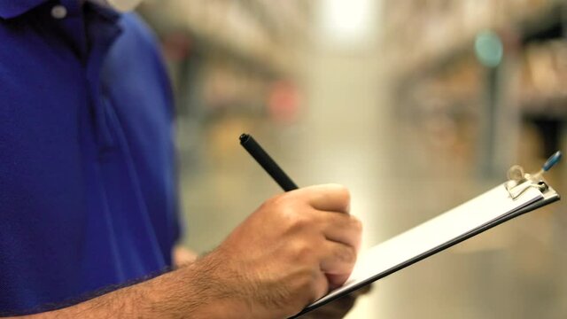 Young worker in blue uniform checklist manage parcel box product in warehouse. Asian man employee holding clipboard working at store industry. Logistic import export concept.