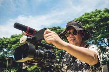 A veteran cameraman recording an outdoor news segment with a medium sized camcorder mounted on a...