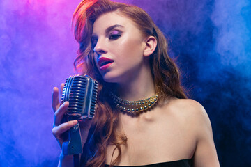Cropped portrait of young female jazz singer isolated over gradient blue purple background in neon...