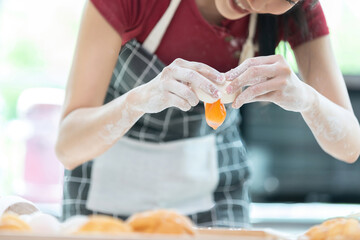 close up housewife or chef hands cracking fresh egg yolk and dropping in a bowl
