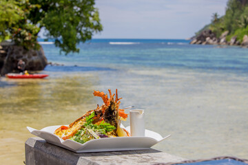 Large lobster steak on a plate against the backdrop of a tropical landscape. Exotic gourmet food by the sea.