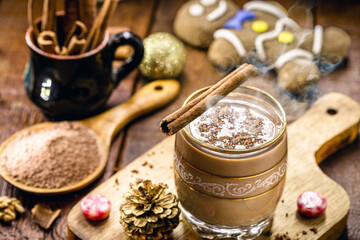 Christmas cup decorated with hot chocolate, cinnamon stick, cocoa and gingerbread man in the background