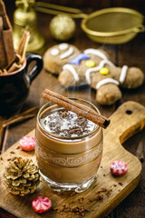 Christmas cup decorated with hot chocolate, cinnamon stick and gingerbread man in the background