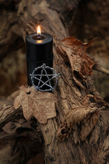 Pentacle amulet and black candle on dark natural autumn forest background. magical esoteric ritual....