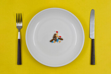 Table setting white plate filled capsules and pills on yellow background