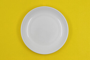 Table setting, empty white plate on yellow background, photo directly above
