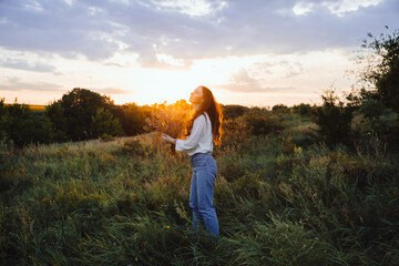 Fototapeta na wymiar Healing Power of, Benefits Of Ecotherapy, Nature Impact Wellbeing. Happy young woman with long hair and a bouquet of wild flowers enjoy nature and life at sunset