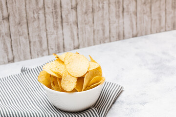 A isolated white bowl of potato chips on top of a napkin with strip pattern