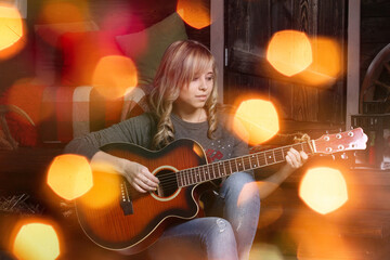 A young charming caucasian blonde woman in a gray sweater and blue jeans playing acoustic guitar on...