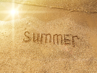 The word Summer is written on the sandy beach