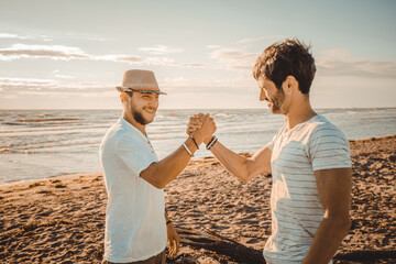 Portrait of two smiling guys on the beach shaking hands - Happy best friends greeting each other...