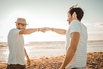 Two caucasian  smiling guys on the beach greeting each other with touch of fist - Meet concept,...