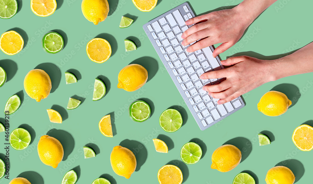 Poster woman using a computer keyboard with fresh lemons and limes overhead view - flat lay