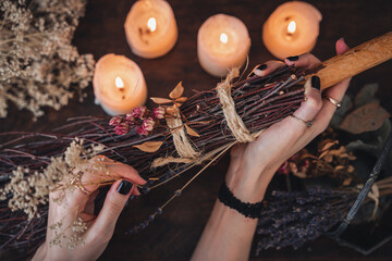 Wiccan witch decorating a DIY besom broom for Samhain celebration. Hand made broom on a dark wooden...