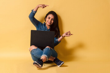 Latinx woman sitting on floor using a laptop pointing with hands and fingers to the side copy space.