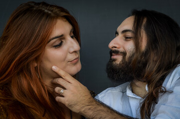 Portrait of a young couple where the young man with beard and long hair caresses the face of the young woman with long red hair